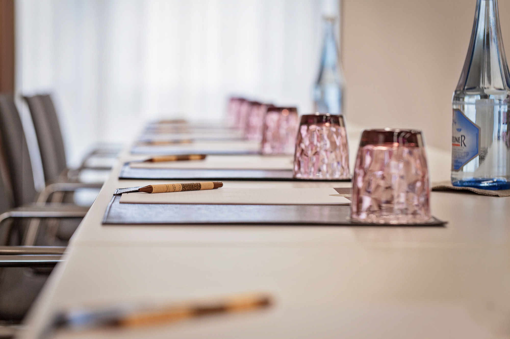 Detailansicht eines gedeckten Konferenztisches im Hotel mit Schreibunterlagen, Gläsern und Wasserflasche